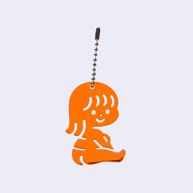Orange acrylic charm of a small cartoon girl sitting down and smiling. It is attached to a ball chain.