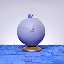 A globe, painted entirely light purple with a closed eye, calm facial expression. A small blue wooden snail rests atop the globe, which sits on a gold base.
