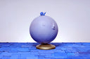 A globe, painted entirely light purple with a closed eye, calm facial expression. A small blue wooden snail rests atop the globe, which sits on a gold base.