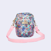 Small crossbody purse with a front pocket and a long strap. Features pastel pink colored fabric detailing, around the zipper and as the handles/straps. Bag has a small "tokidoki" nameplate on the upper center and is covered completely in a busy colorful pattern featuring tokidoki characters with with galactic and sci fi imagery.