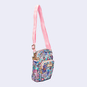 Small crossbody purse with a front pocket and a long strap. Features pastel pink colored fabric detailing, around the zipper and as the handles/straps. Bag has a small "tokidoki" nameplate on the upper center and is covered completely in a busy colorful pattern featuring tokidoki characters with with galactic and sci fi imagery.