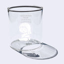 Small clear glass cup with a cartoon graphic on the front of a small girl sitting on the ground and smiling.