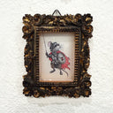 An ornate, vintage-style rectangular picture frame with a highly detailed baroque design in dark brown and gold, featuring a hand-painted illustration of a mouse dressed as a knight with a red cape, mounted on a textured white wall.