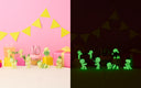 Glowing green figures on a dark background with pink decorations and yellow flags on a light background.