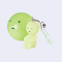 Small Smiski figure, sitting with their knees pulled into their chest. They have a clear keychain attached via metal hardware that says "smiski". FIgure sits in front of a capsule that is a large round Smiski head.