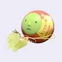 Small keychain of a Smiski, a simplistic round headed green character with a small face. It lays on its stomach with its head propped up in its hands, next to its capsule packaging.