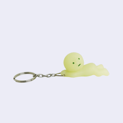Smiski, attached to a keychain by their hands where they look as if they are grabbing and holding onto the keychain, with the rest of their body hanging off.
