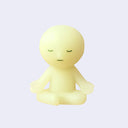 Small figure of Smiski - a character with a round head and stick-like body, sitting in a meditative pose with their eyes closed, legs crossed and palms open on their knees.