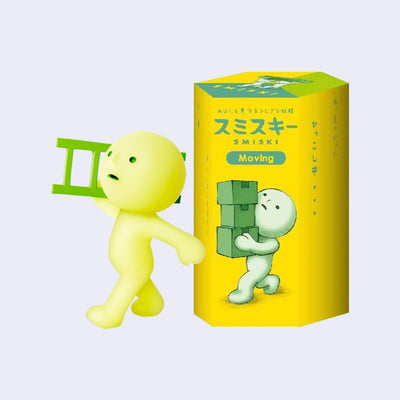 A small plastic character, light green with a circular head and human like body. It walks purposefully and holds a ladder over its shoulder. It stands next to its product packaging.