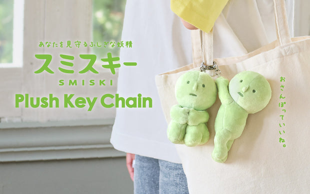 Green plush keychains attached to a tote bag with SMISKI branding.