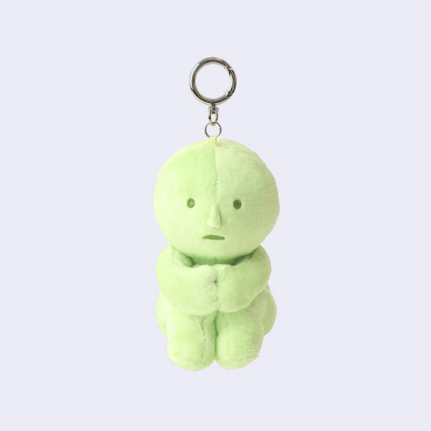 Green plush keychain of Smiski, sitting with its knees pulled into its chest.