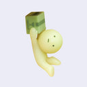 Small figure of Smiski - a character with a round head and stick-like body, dangling from a box they hold onto.