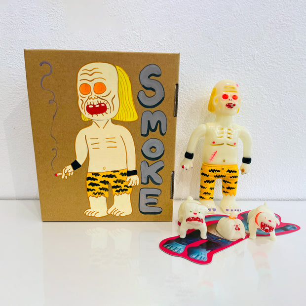 Light yellow soft vinyl figure of a shirtless man, balding but with long blonde hair. He smokes a cigarette and wears patterned pants. 3 smoking dogs stand in front of him, all stand beside a painted box.