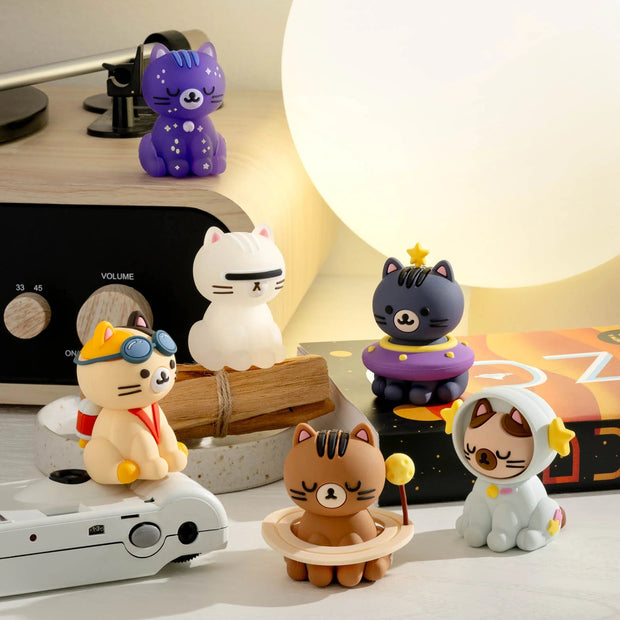 Set of small space themed cat figurines on a desk with a lamp in the background