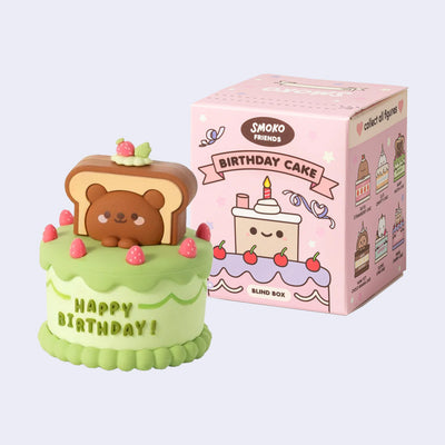 Cute birthday cake figurine with a bear on top next to its packaging box.