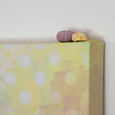 Side of a yellow painted canvas, with a few sea shells resting atop it.