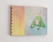Painting of an anthropomorphized green mountain, sitting and taking a bite out of a rounded flower. Atop its head is a crescent moon and the background is light blue/yellow with an additional orange scalloped panel.