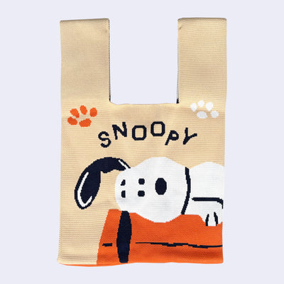 Beige tote bag with Snoopy design, of him laying on an orange dog house and looking at the viewer. Text overhead says "Snoopy"