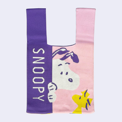 Snoopy-themed fabric tote bag with a pink and purple coloring. Snoopy peeks out from the purple section and looks onto Woodstock.