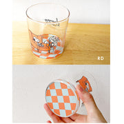 Glass tumbler with checkered design at the bottom that can be seen from overhead and below, and a graphic of Snoopy sitting in a chair.