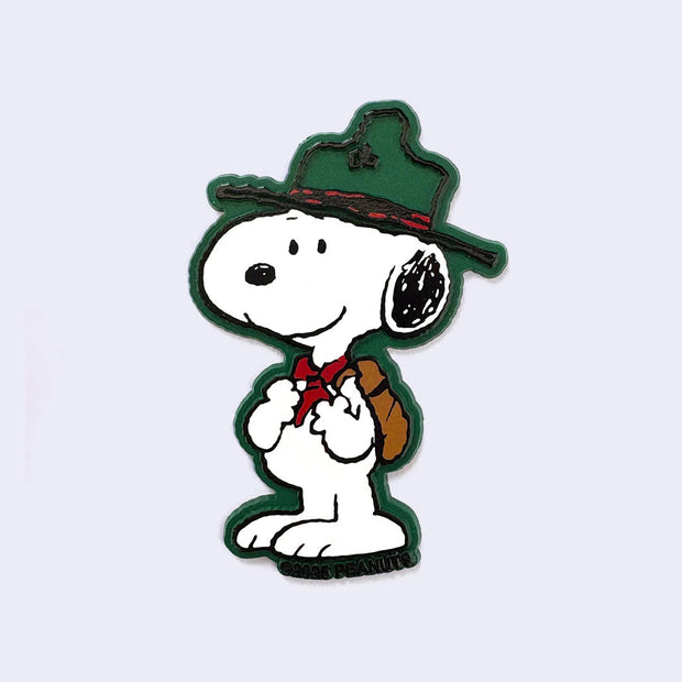 Die cut refrigerator magent of Snoopy, dressed as a Beagle Scout with an outdoors hat, red bandana scarf and a brown backpack. Background outline is a forest green.