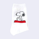 White crew socks with a graphic of Snoopy, sitting and smiling atop of his red dog house on the side of the sock. Only the top part of the dog house is seen.