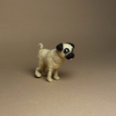 A small felted wool dog figurine, resembling a pug, standing on a plain brown studio background.