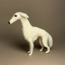 A handcrafted felted wool figurine of a slender white dog, a Borzoi, standing in profile against a solid warm brown background.