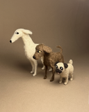 Three felt animal figurines, including a white dog, a brown dog, and a pug, arranged on a plain beige studio background.
