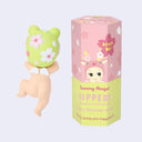 Blind box of a Sonny Angel Cherry Blossom Hipper Series, next to one of the figure options, a baby wearing a frog hat with cherry blossoms on it.