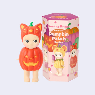 Figurine of a Sonny Angel dressed as a pumpkin, with a cat shaped pumpkin hat. They stand in front of their fall themed product packaging.