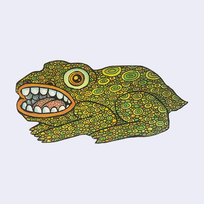 Die cut wooden sculpture of a frog like creature with an open mouth showing teeth. Its skin is comprised of many small circles of green and yellow.