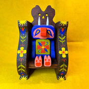 Colorful wooden figure of a cute, blue troll monster sitting in a wooden throne.