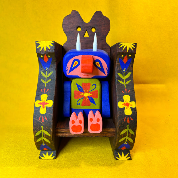 Colorful wooden figure of a cute, blue troll monster sitting in a wooden throne.