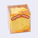A yellow cheese-shaped squishy toy inside a clear plastic box with orange and white graphics and the text 'squeeze cheese' and 'TRY ME!'.