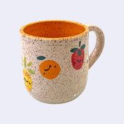 Ceramic mug with spotted finishing and an earthy brown exterior and orange interior. On the outside are painted on cartoon style fruits, with simple expressions.