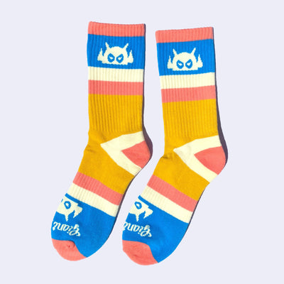 Striped salmon pink, blue, cream and yellow socks with a cream colored cartoon robot head on them and cream colored heels and toes. The robot head decorates the cuff end of each sock so that it peeks out when you wear sneakers.