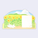 Back view of die cut illustrated greeting card, with a white dog playing in a sunflower field with a small white square where words can be written.