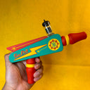 Colorful toy gun with 'Sun-Ray' retro branding held against a yellow background
