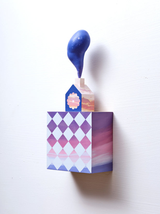 Small square wood panel painted like a pink and purple sunset with light blue diamond patterning overlayed on top, akin to a quilt tile design. Atop of it is a carved wooden house with a large painted flower on the front and a thick plume of smoke coming out the top.