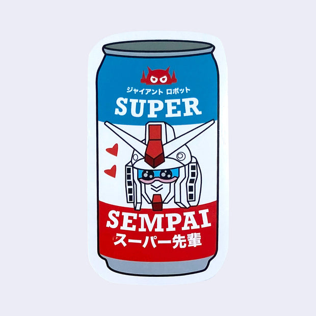 Die cut sticker of a can of soda, red white and blue with a graphic of a smiling kawaii style gundam. 