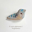 Ceramic sculpture of a tiny bird, blue and brown with hollowed out eyes.