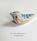 Ceramic sculpture of a tiny bird, blue and brown with hollowed out eyes.