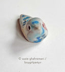 Ceramic sculpture of a tiny bird, blue and brown with hollowed out eyes.