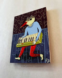 thin wood panel with a stylized illustration of a bird playing a keyboard on a patterned background