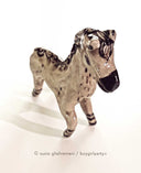 Ceramic horse figurine, beige in color with detailing of purple for its mane, eyes, hooves and snout.