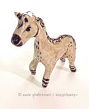 Ceramic horse figurine, beige in color with detailing of purple for its mane, eyes, hooves and snout.