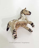 Ceramic horse figurine, beige in color with detailing of purple for its mane, eyes, hooves and snout.