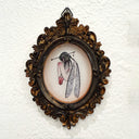 An ornate oval framed art piece mounted on a textured white wall. The frame is dark brown with gilded detailing.