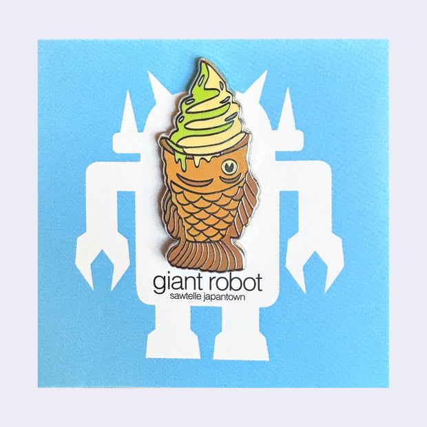 Die cut sticker of a taiyaki fish shaped waffle pastry with a swirl of matcha and vanilla soft serve in it, dripping slightly. Below is text that reads "taiyaki ice cream / Giant Robot"
